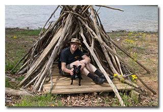 A man and a dog inside a log teepee